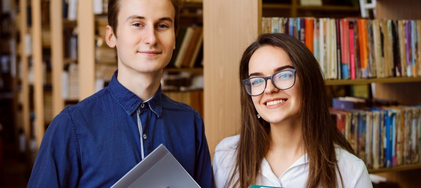Dwoje uśmiechniętych studentów stoi w bibliotece na tle regałów