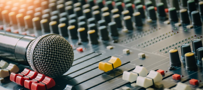 Mikrofon dynamiczny leżący na konsolecie. Konsoleta czarna, na nim przyciski w kolorze czarnym, żółtym, czerwonym i białym 